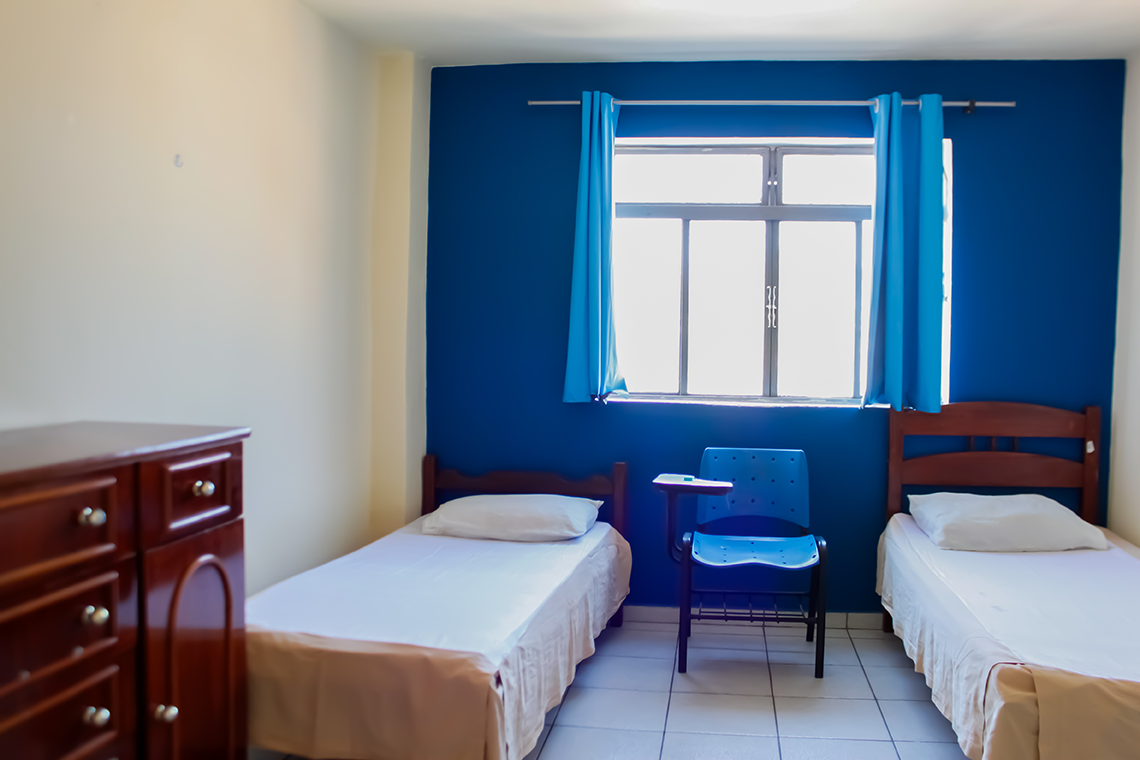 foto de um quarto com duas camas de solteiro, uma janela e uma cadeira