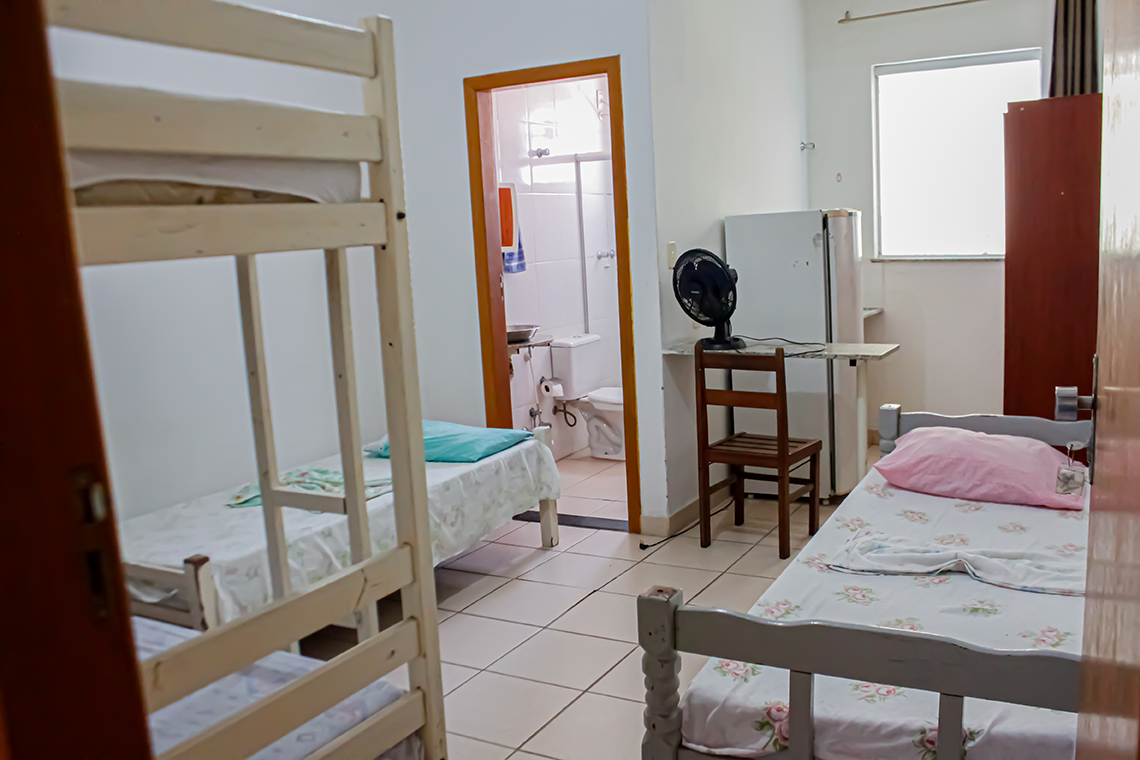 imagem de entrada de um quarto onde se ve uma beliche na sua esquerda e duas camas de solteiro normais