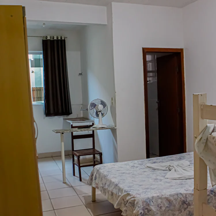 mostra a visao de entrada de um quarto onde se ve a cama de casal um ventilador sobre uma bancada