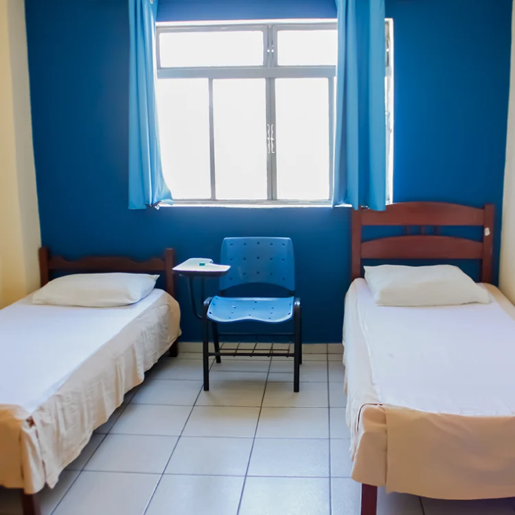 foto de um quarto com duas camas de solteiro, uma janela e uma cadeira